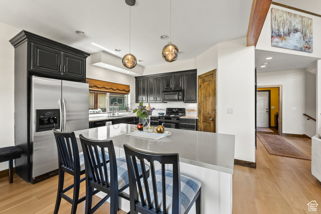 Kitchen featuring light hardwood / wood-style floors, stainless steel fridge, range, a kitchen island, and hanging light fixtures