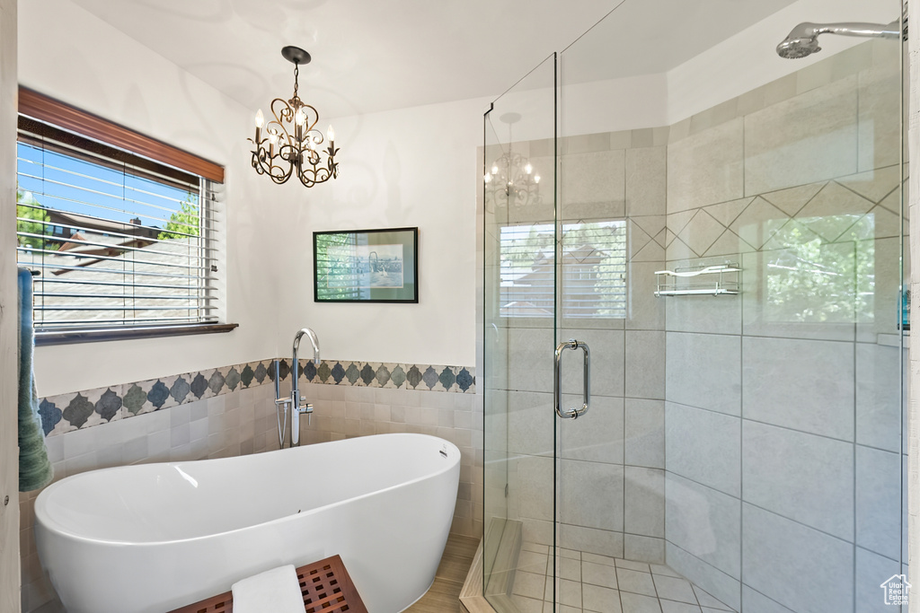 Bathroom featuring separate shower and tub, a chandelier, and tile walls