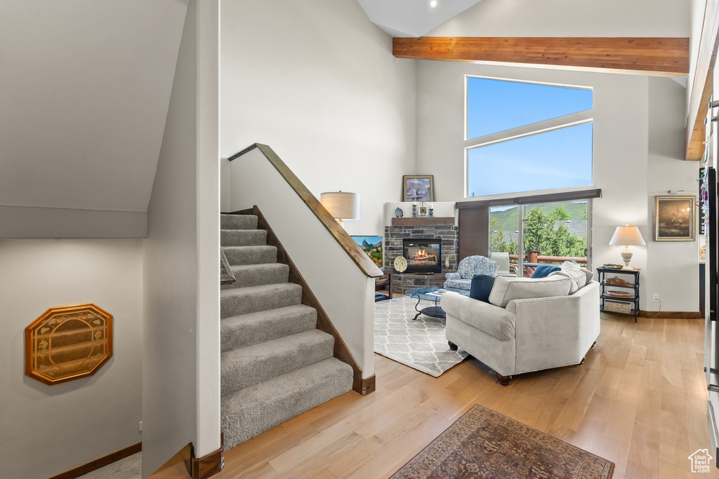 Living room featuring beamed ceiling, high vaulted ceiling, light wood-type flooring, and a stone fireplace