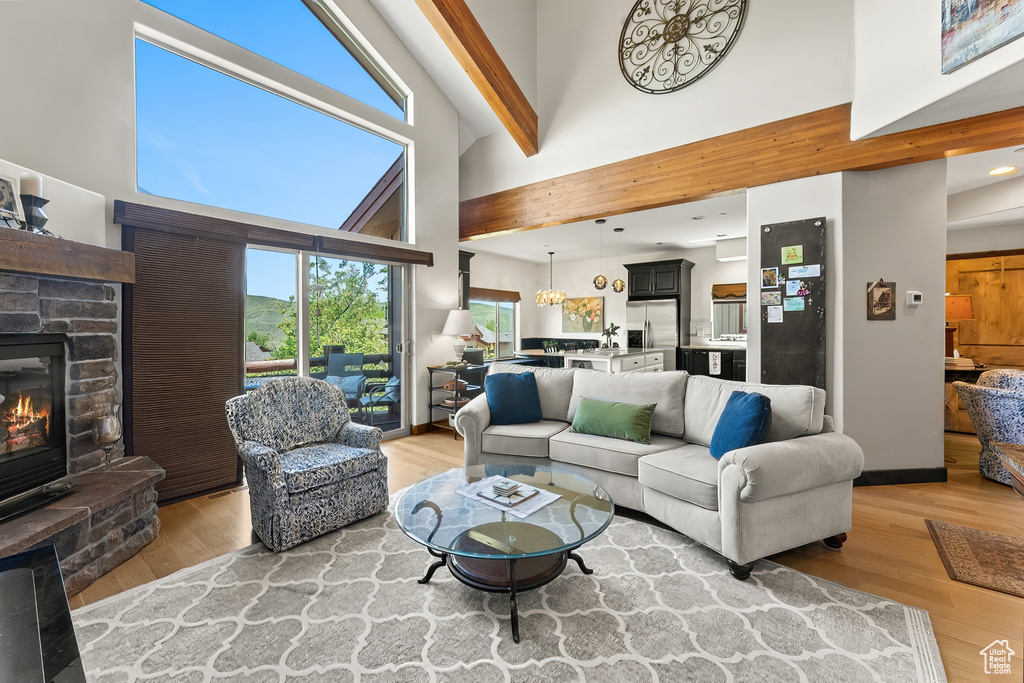 Living room featuring hardwood / wood-style flooring, beam ceiling, a high ceiling, a stone fireplace, and a chandelier