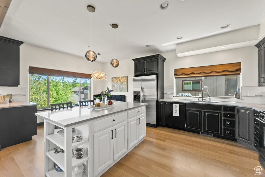 Kitchen with light hardwood / wood-style floors, backsplash, black dishwasher, white cabinetry, and stainless steel fridge