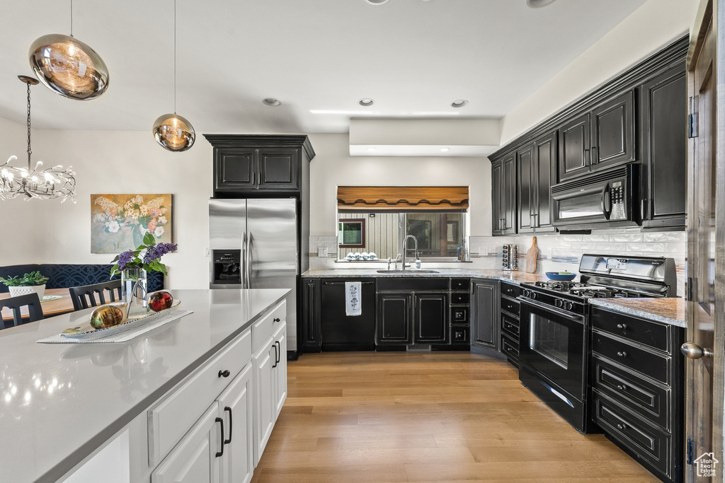 Kitchen featuring white cabinetry, hanging light fixtures, light wood-type flooring, black appliances, and tasteful backsplash