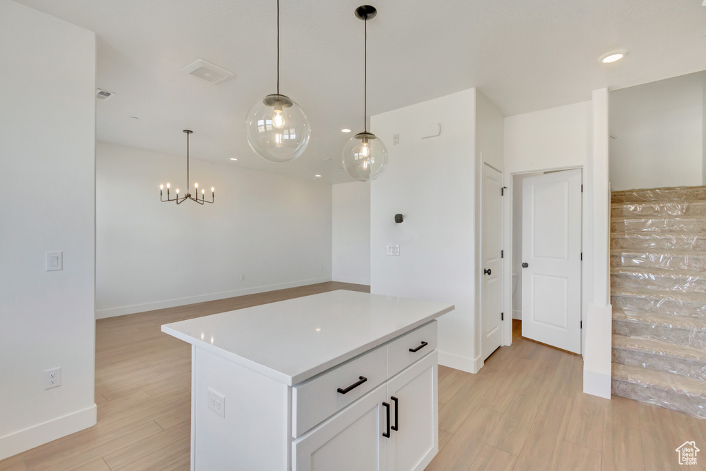 Kitchen featuring white cabinetry, light hardwood / wood-style flooring, a notable chandelier, decorative light fixtures, and a center island