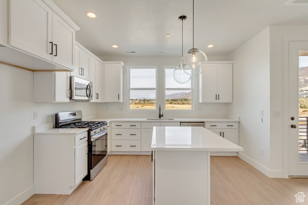 Kitchen with appliances with stainless steel finishes, a kitchen island, white cabinetry, decorative light fixtures, and light hardwood / wood-style flooring