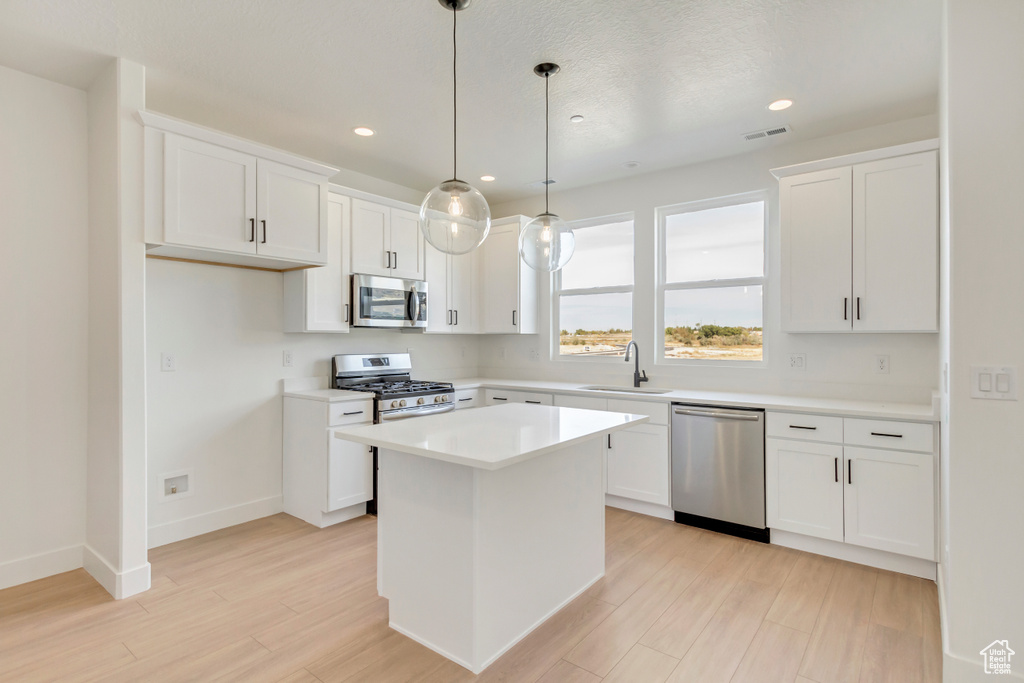 Kitchen with sink, a kitchen island, appliances with stainless steel finishes, and white cabinetry