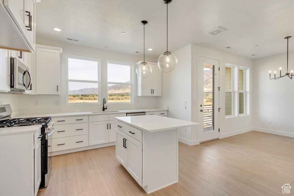 Kitchen featuring a kitchen island, white cabinetry, gas range gas stove, sink, and decorative light fixtures