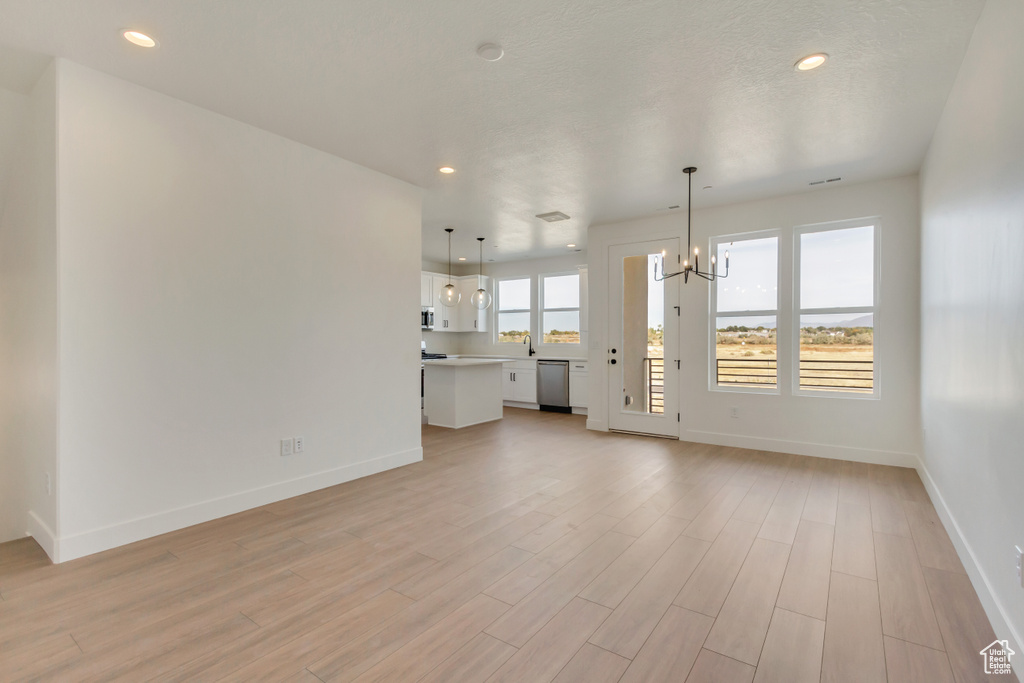 Unfurnished living room featuring an inviting chandelier and light hardwood / wood-style floors