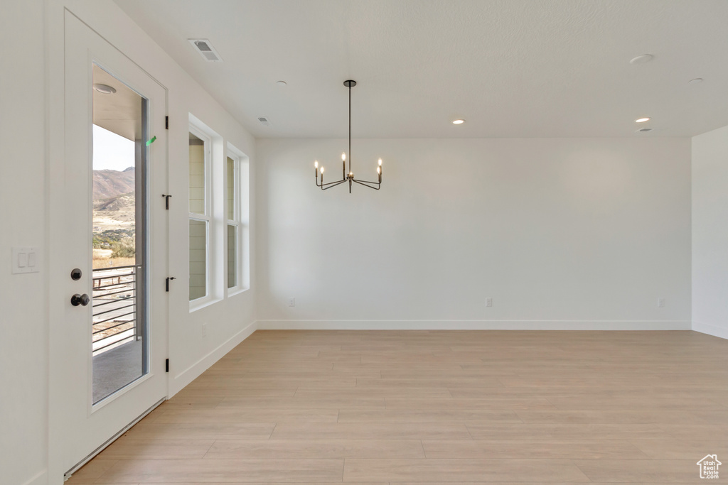 Unfurnished room featuring light hardwood / wood-style flooring, a notable chandelier, and a wealth of natural light