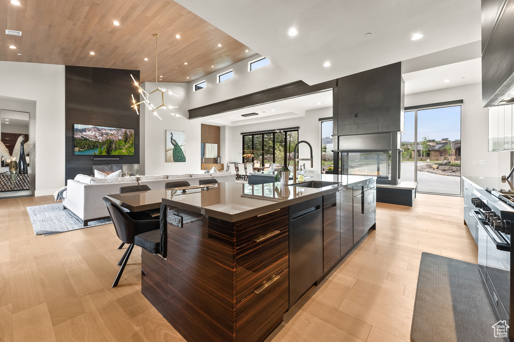 Kitchen featuring a multi sided fireplace, dishwasher, sink, a spacious island, and decorative light fixtures