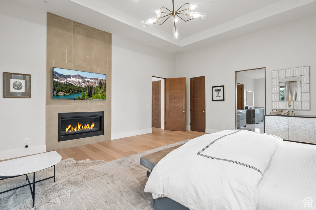 Bedroom with a tiled fireplace, a chandelier, hardwood / wood-style floors, and a tray ceiling