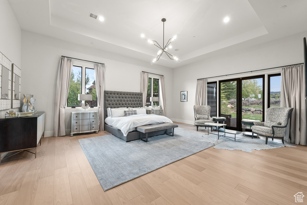 Bedroom featuring a notable chandelier, a raised ceiling, and light wood-type flooring