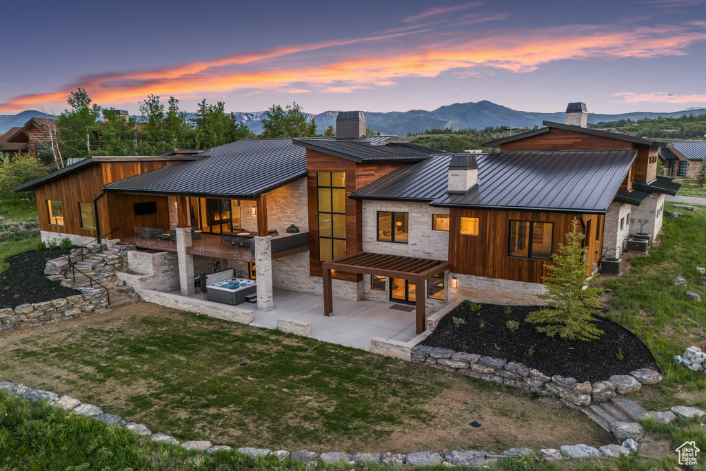 Back house at dusk with a lawn, a patio, and central AC unit