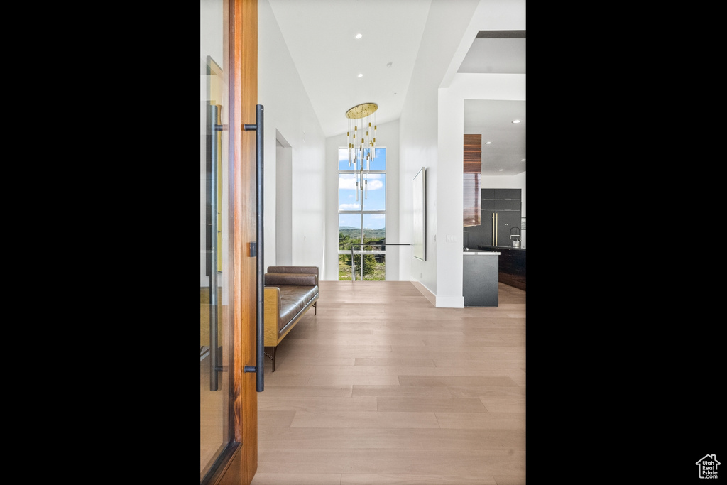 Corridor with light hardwood / wood-style flooring, a chandelier, and a high ceiling