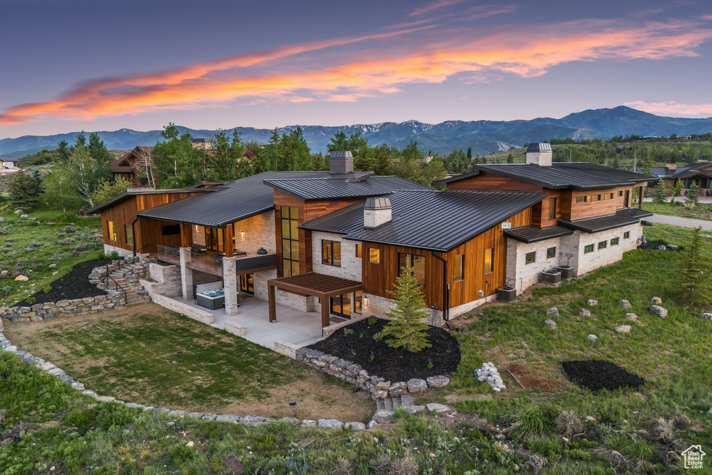 Back house at dusk featuring a patio, a mountain view, and a lawn