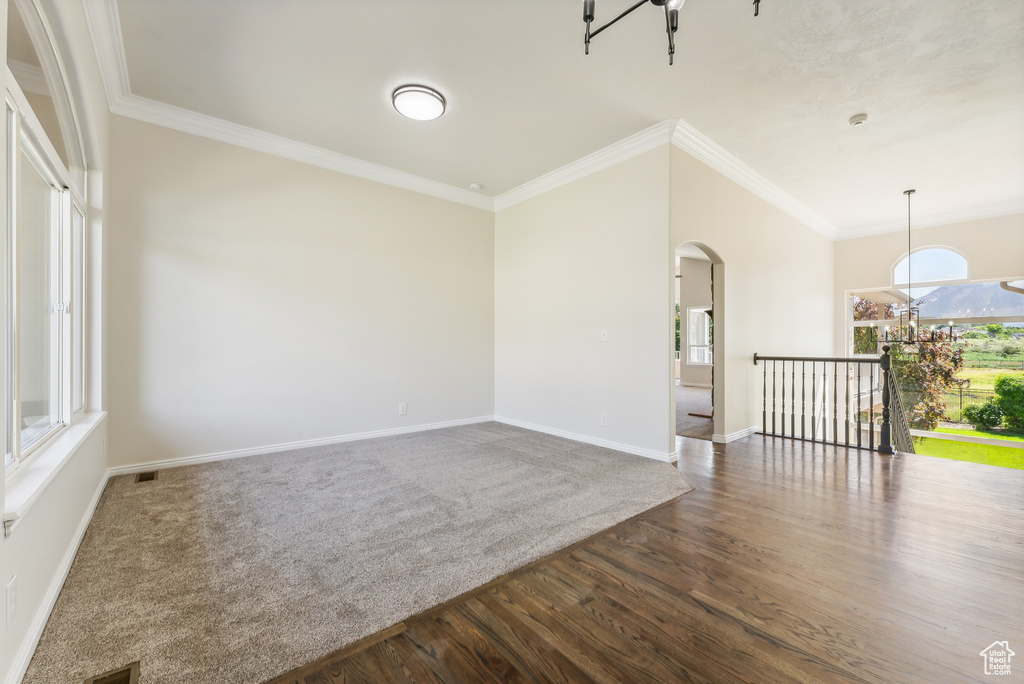 Spare room with a notable chandelier, ornamental molding, and dark wood-type flooring