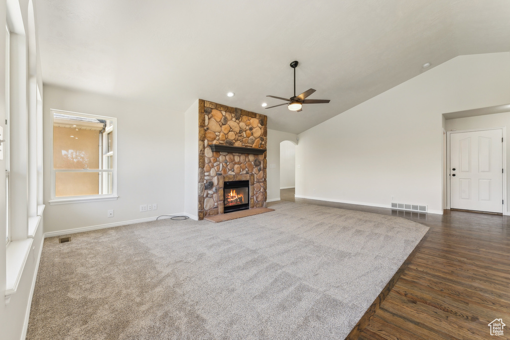 Unfurnished living room with ceiling fan, dark colored carpet, vaulted ceiling, and a fireplace