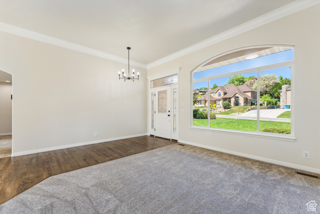 Empty room with dark wood-type flooring, a chandelier, and crown molding