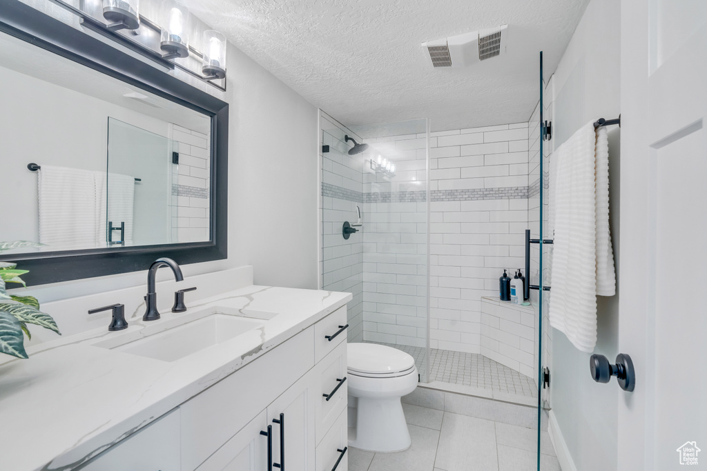 Bathroom with walk in shower, a textured ceiling, tile floors, toilet, and vanity