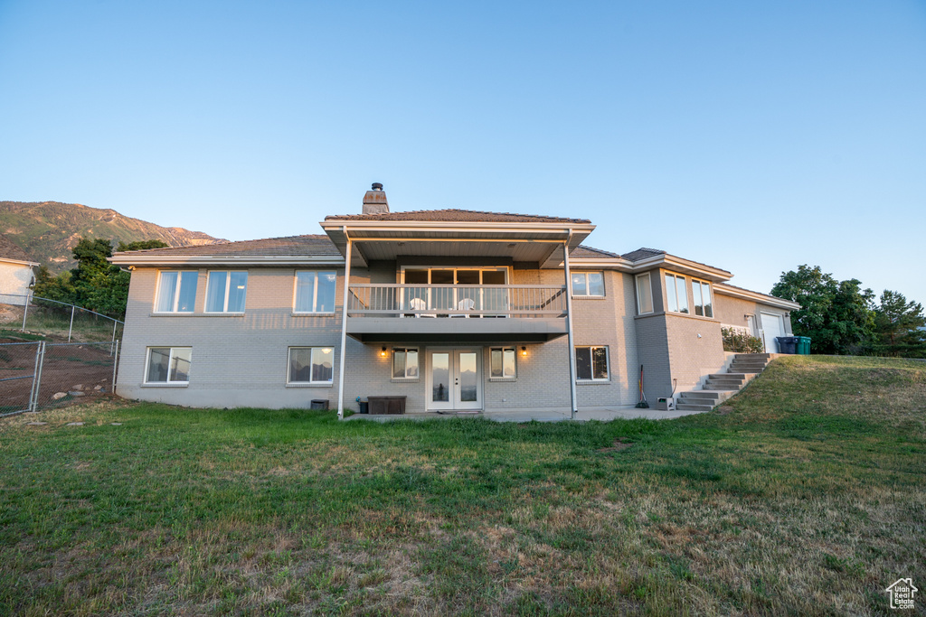 Back of property with a mountain view, french doors, a balcony, a yard, and central air condition unit