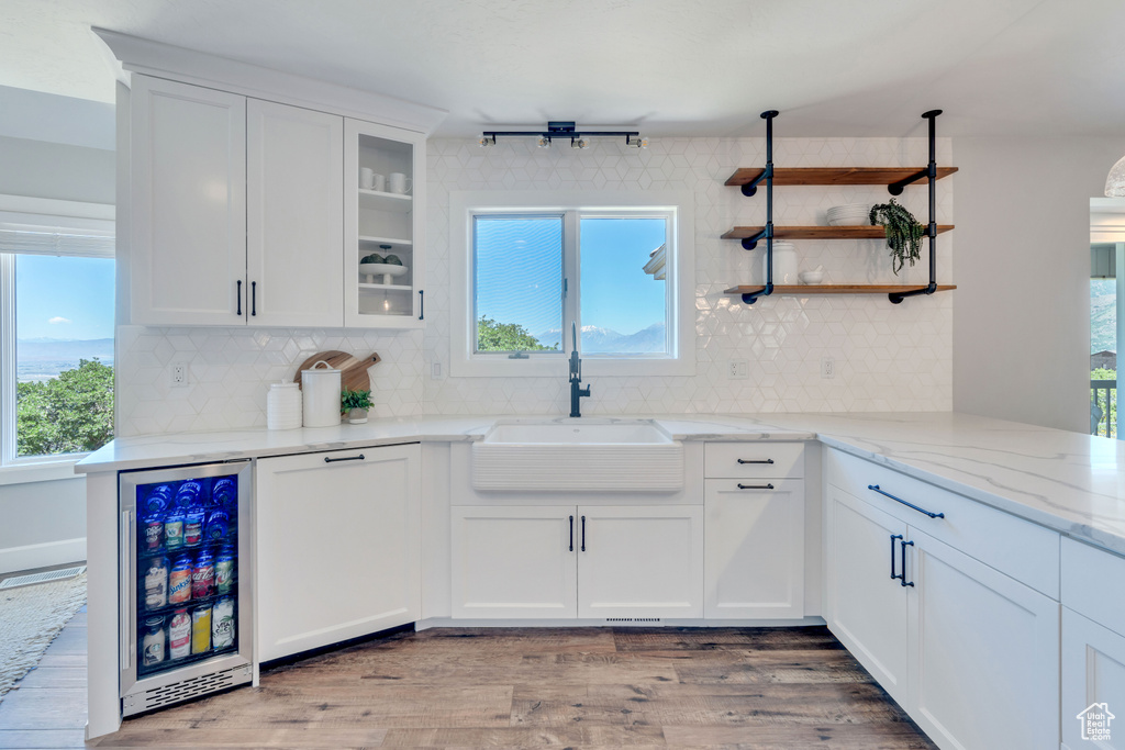 Kitchen featuring white cabinetry, light stone countertops, beverage cooler, wood-type flooring, and sink