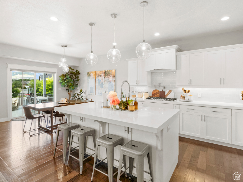 Kitchen featuring an island with sink, decorative light fixtures, backsplash, and hardwood / wood-style floors