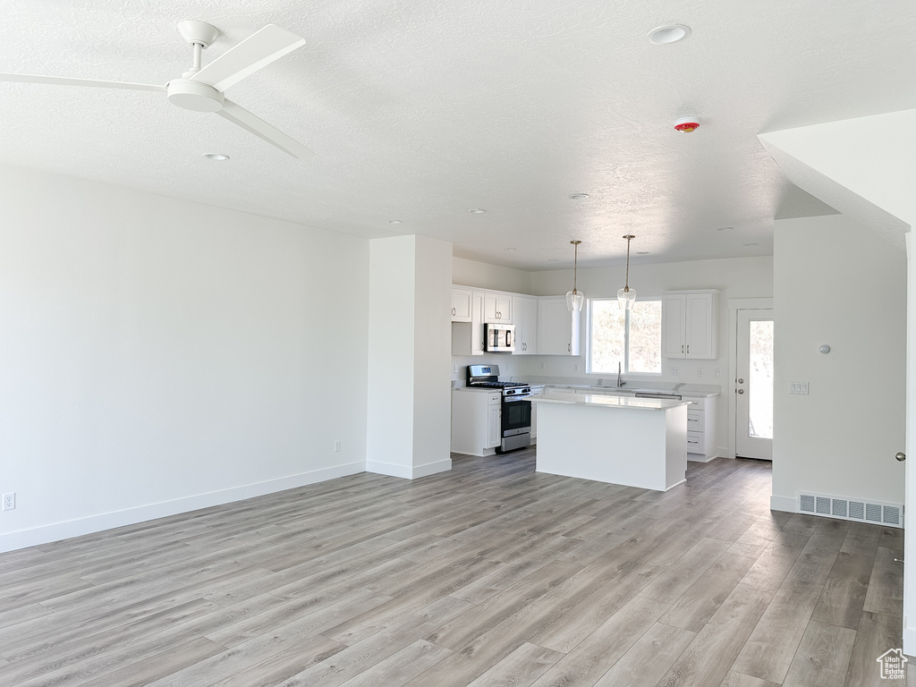 Kitchen featuring white cabinets, a kitchen island, appliances with stainless steel finishes, light hardwood / wood-style flooring, and decorative light fixtures