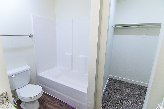 Bathroom with washtub / shower combination, hardwood / wood-style floors, and toilet