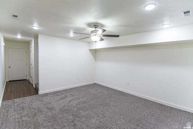 Empty room featuring ceiling fan, dark colored carpet, and a textured ceiling