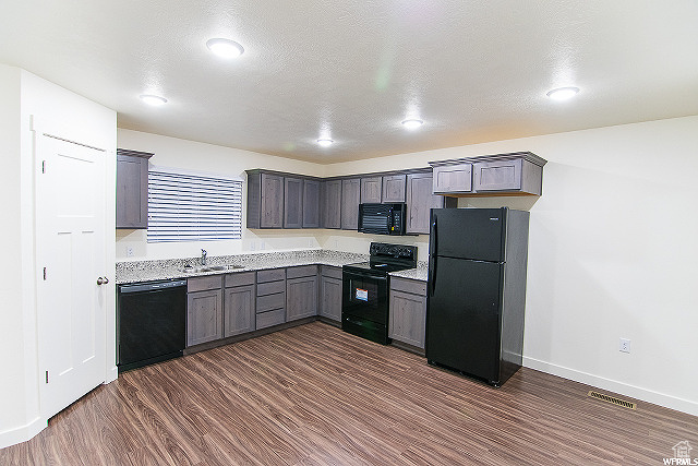 Kitchen featuring dark wood-type flooring, sink, black appliances, and a textured ceiling