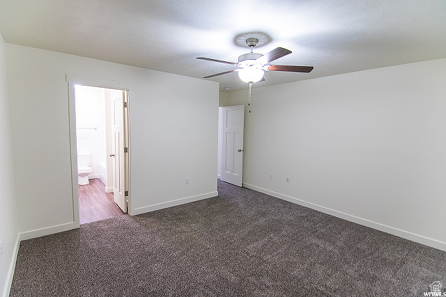 Unfurnished bedroom featuring ceiling fan, dark carpet, and ensuite bathroom