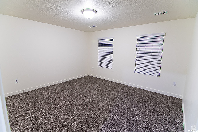 Empty room with a textured ceiling and dark carpet