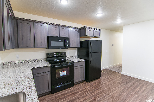 Kitchen featuring light stone countertops, black appliances, dark wood-type flooring, dark brown cabinetry, and a textured ceiling