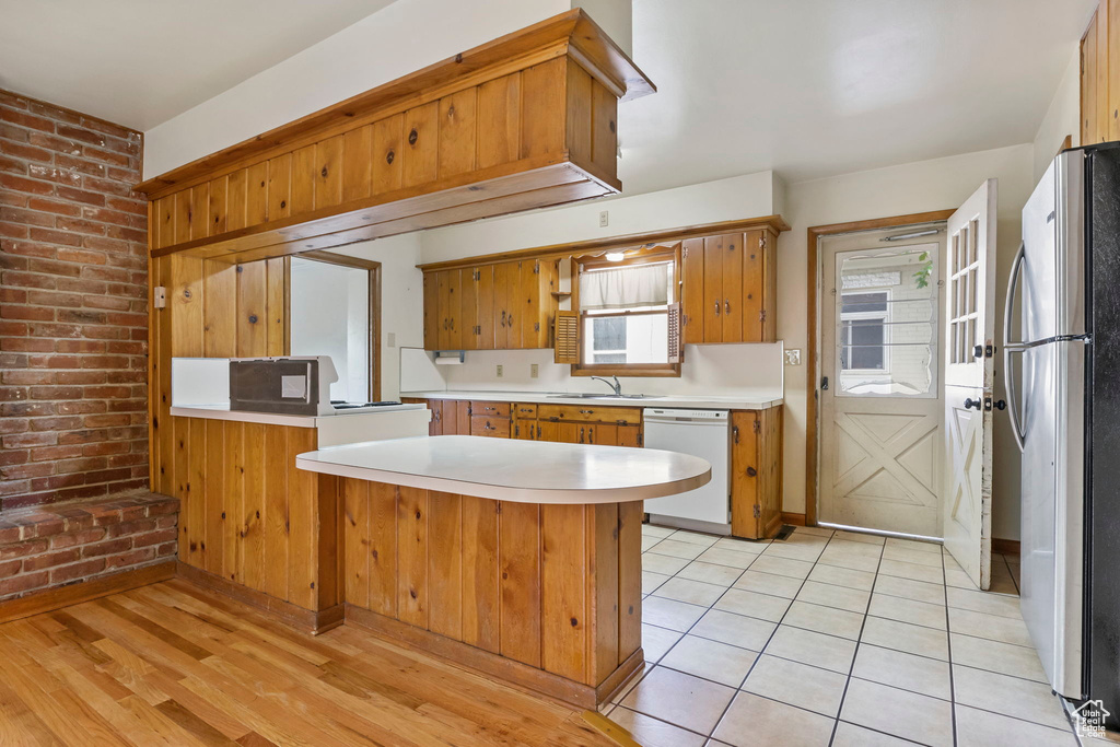 Kitchen with stainless steel refrigerator, kitchen peninsula, dishwasher, light wood-type flooring, and sink