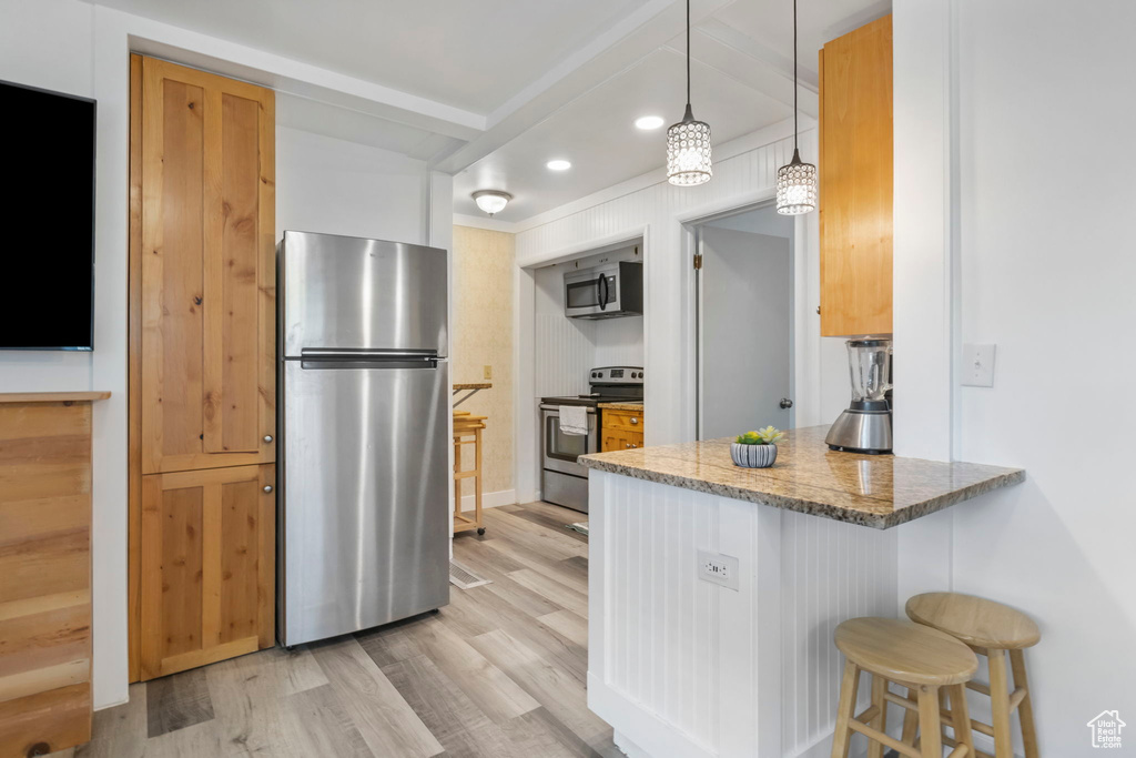 Kitchen with light hardwood / wood-style floors, stainless steel appliances, kitchen peninsula, stone countertops, and a breakfast bar