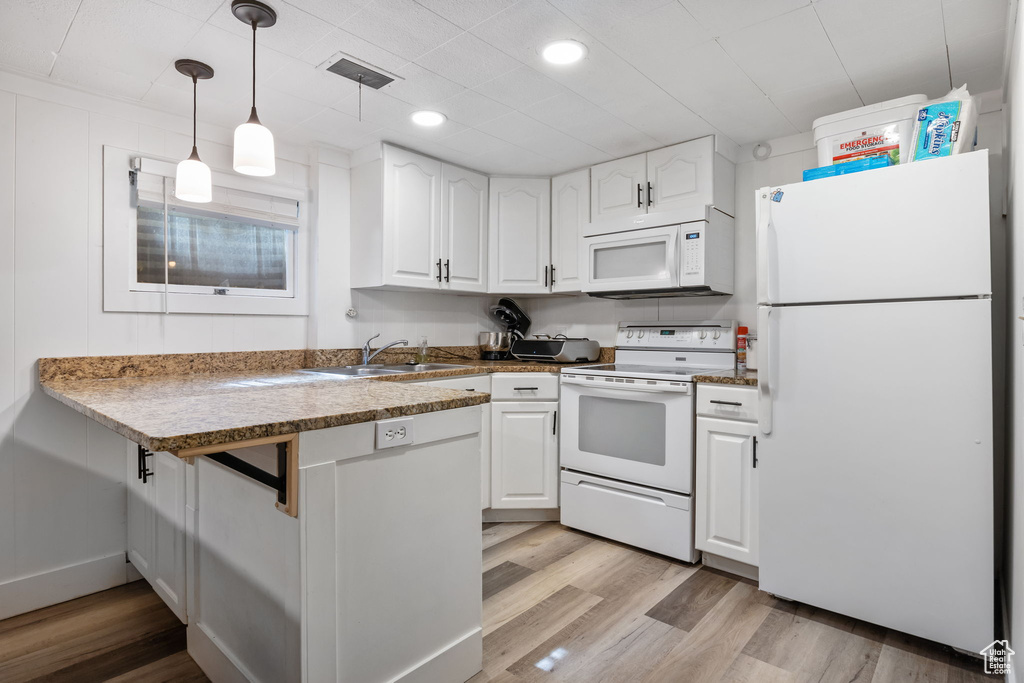 Kitchen featuring light hardwood / wood-style flooring, white appliances, hanging light fixtures, sink, and white cabinetry