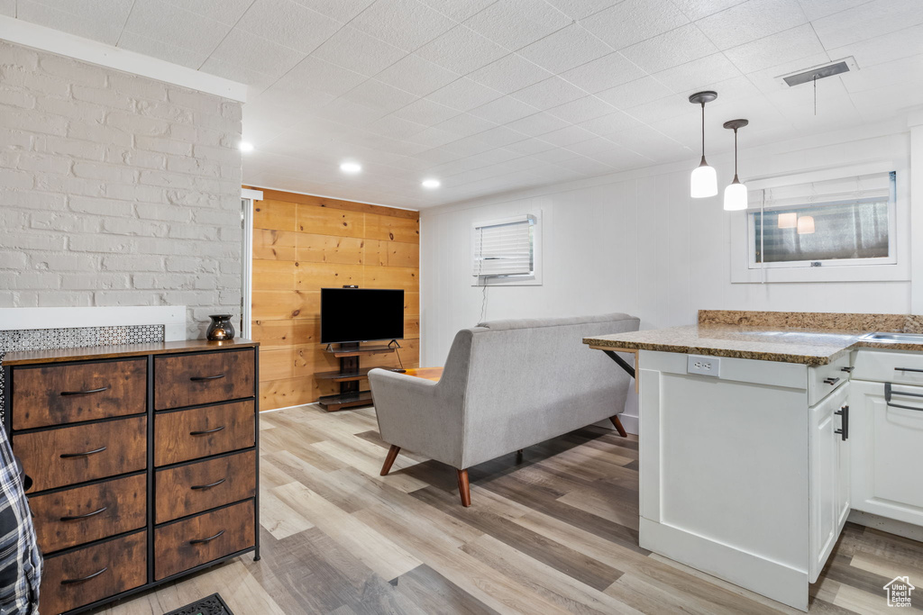 Kitchen featuring decorative light fixtures, light stone counters, light wood-type flooring, white cabinets, and wooden walls