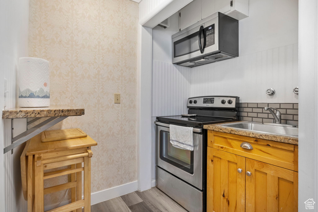 Kitchen with stainless steel appliances, light hardwood / wood-style flooring, tasteful backsplash, and sink