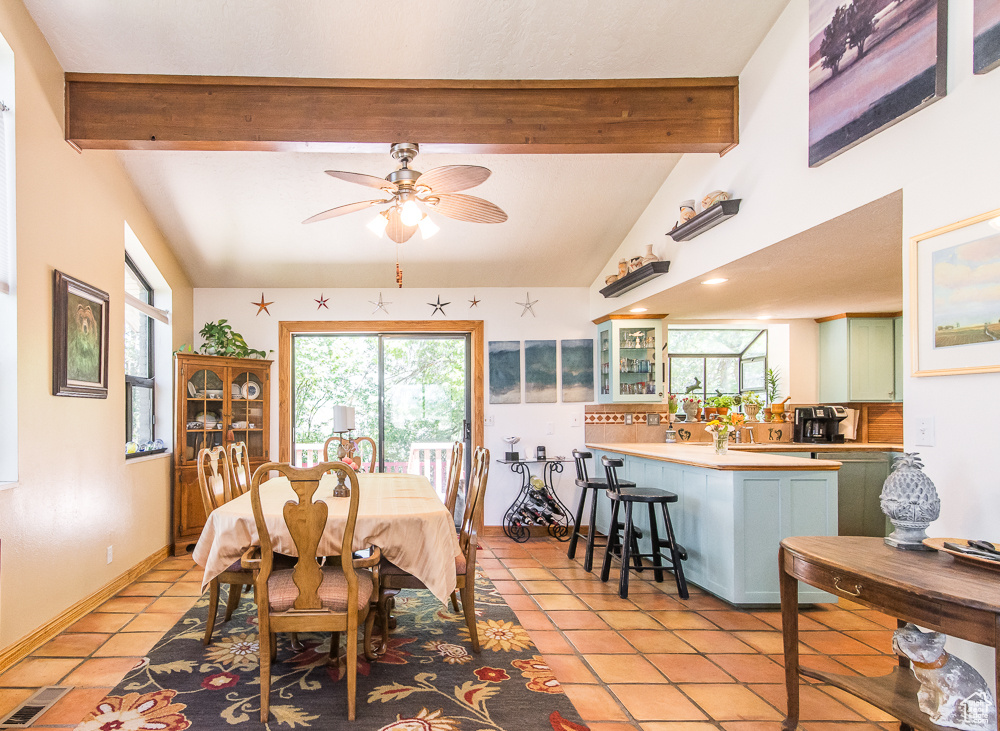 Tiled dining room featuring a healthy amount of sunlight, vaulted ceiling with beams, and ceiling fan