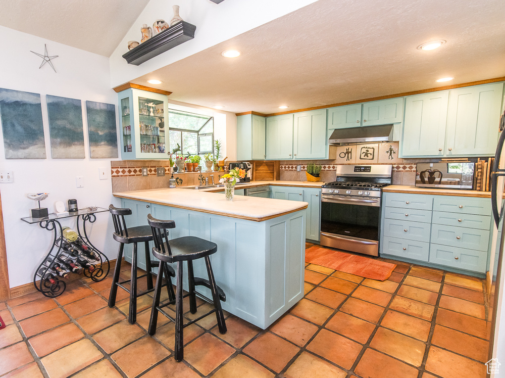 Kitchen with backsplash, kitchen peninsula, gas range, and light tile floors