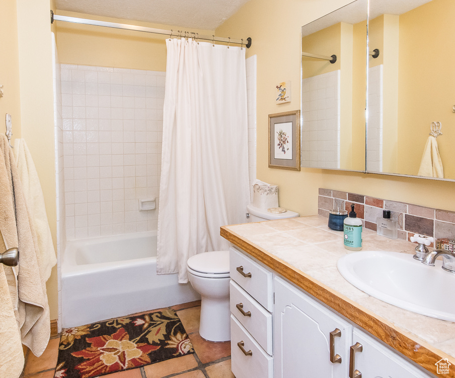 Full bathroom featuring tasteful backsplash, vanity with extensive cabinet space, shower / bath combo, tile floors, and toilet