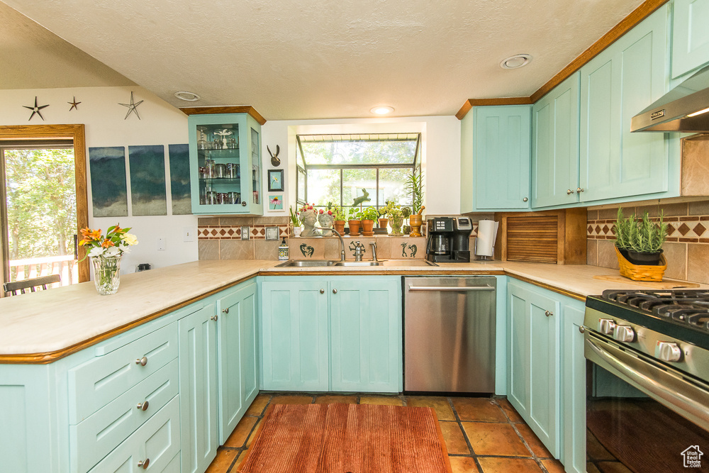 Kitchen with wall chimney range hood, tasteful backsplash, tile floors, appliances with stainless steel finishes, and sink