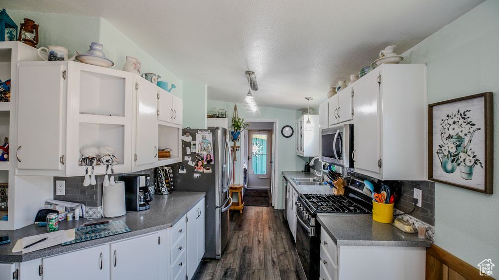 Kitchen with stainless steel appliances, decorative light fixtures, dark hardwood / wood-style flooring, backsplash, and white cabinetry