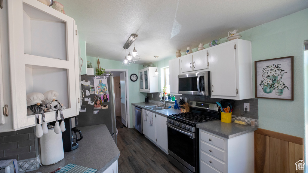 Kitchen featuring decorative light fixtures, dark wood-type flooring, appliances with stainless steel finishes, and tasteful backsplash