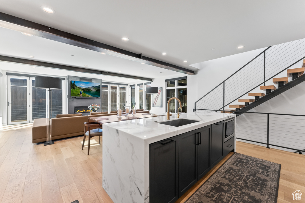 Kitchen with an island with sink, sink, light stone counters, and beam ceiling