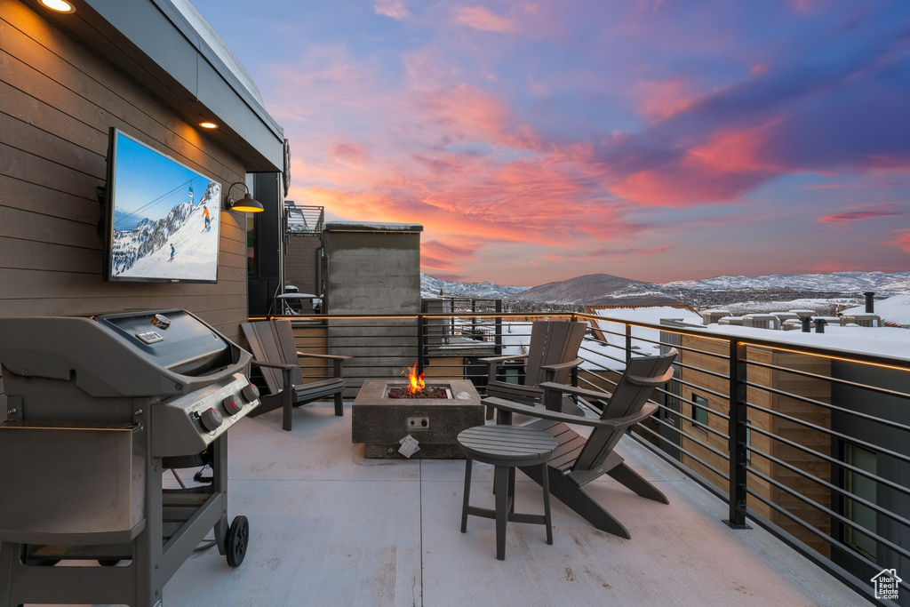 Snow covered patio with a mountain view, a fire pit, a balcony, and grilling area