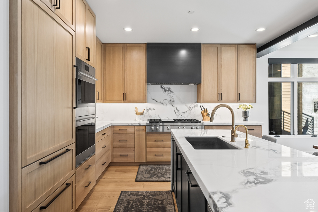 Kitchen with light stone countertops, fume extractor, light hardwood / wood-style floors, light brown cabinetry, and sink