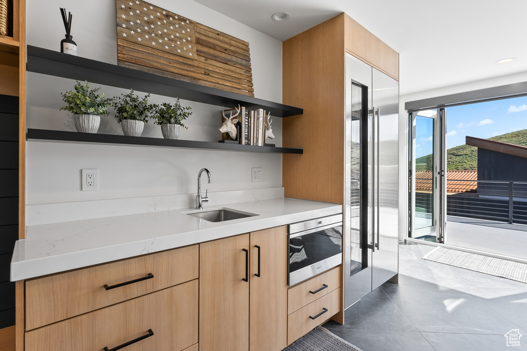 Kitchen featuring sink, dark tile flooring, light stone counters, and light brown cabinets