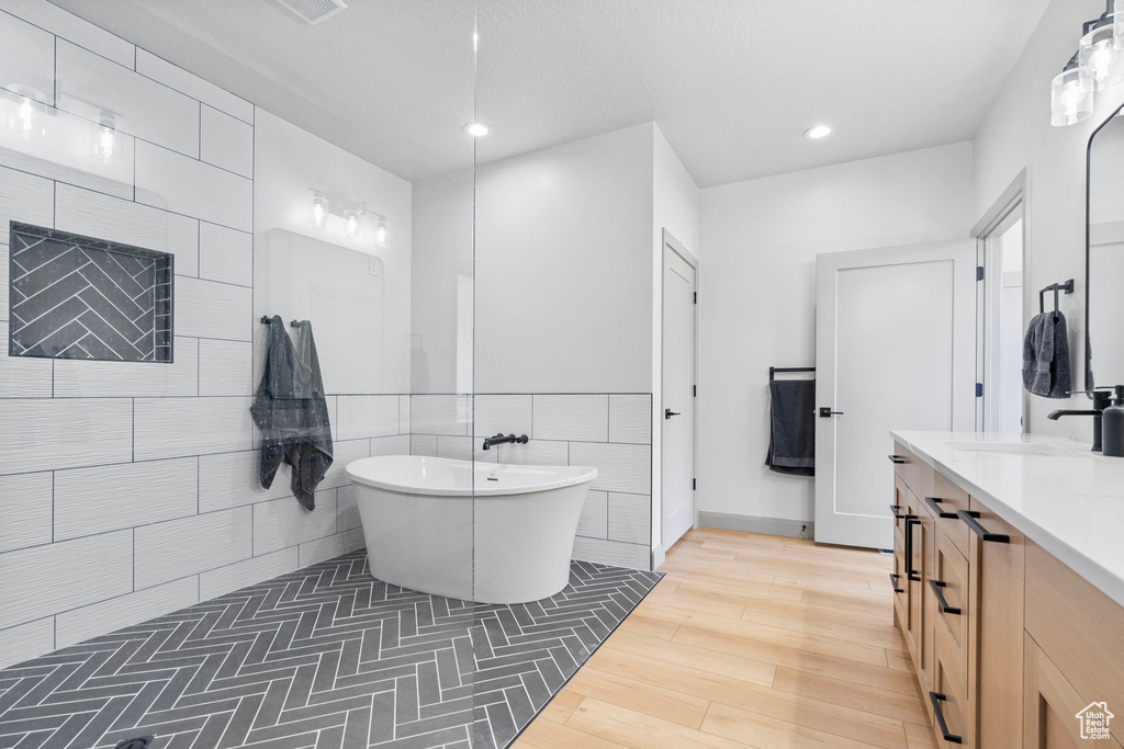 Bathroom with tile walls, a bath, vanity, and hardwood / wood-style floors