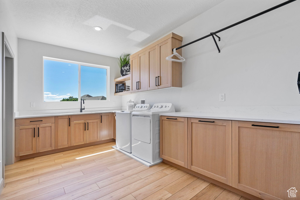 Clothes washing area featuring independent washer and dryer, hookup for a washing machine, light wood-type flooring, a textured ceiling, and cabinets