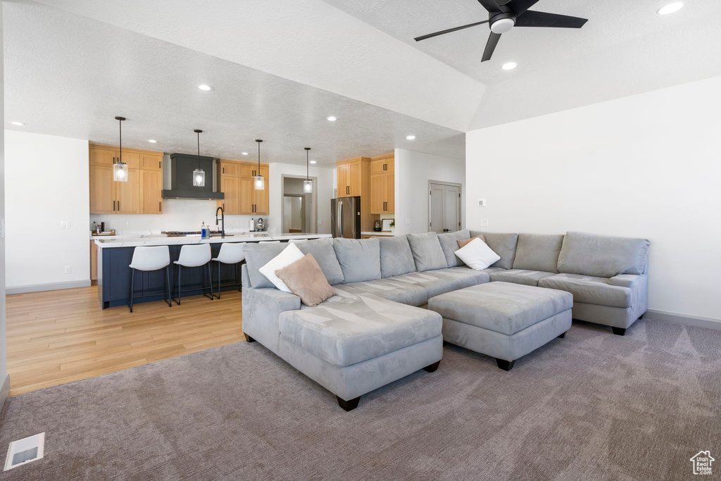 Living room featuring ceiling fan, light hardwood / wood-style flooring, lofted ceiling, and sink